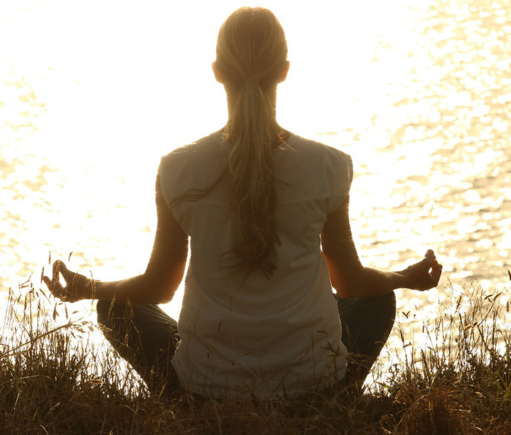 Silhouette of a woman meditating next to a body of water.