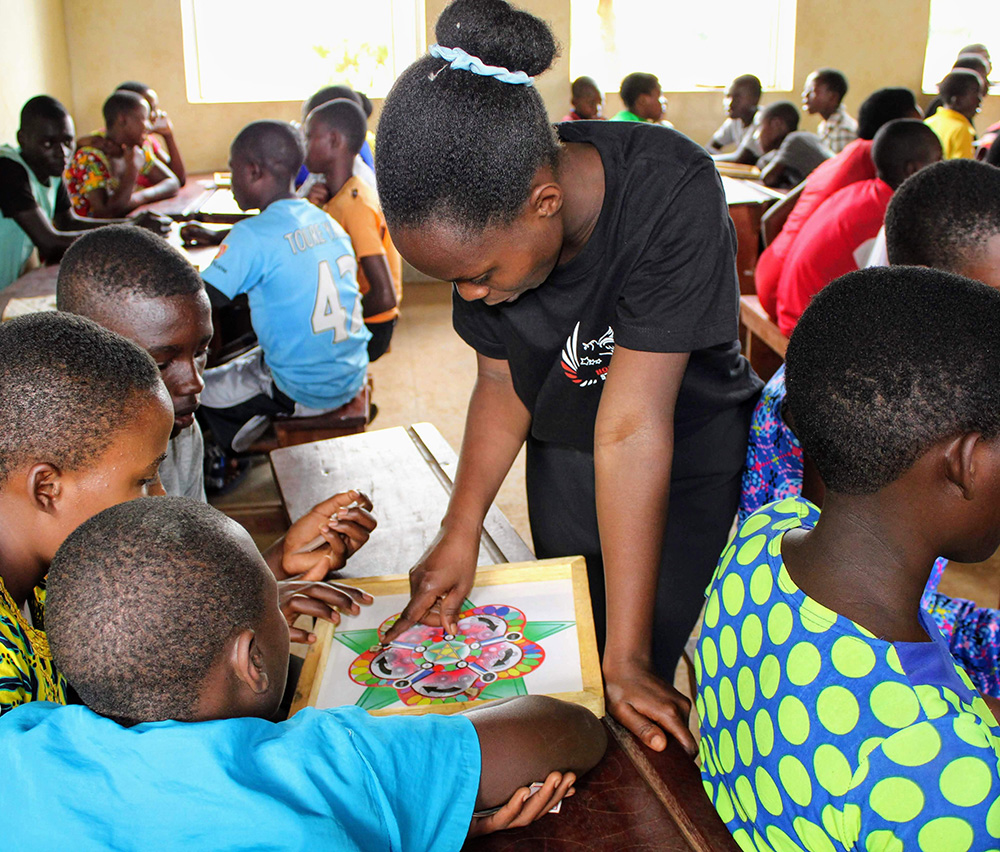 Tisiya Mahoro, standing, helps students at Kinakyeitaka Primary School in Uganda play the 5 STA-Z board game developed by UW–Madison engineering students.